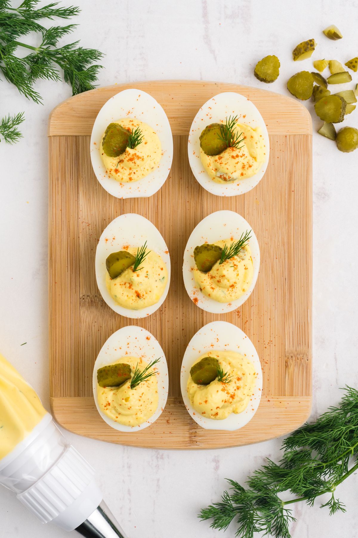 Pickled deviled eggs on a cutting board garnished with diced dill pickle and fresh dill.