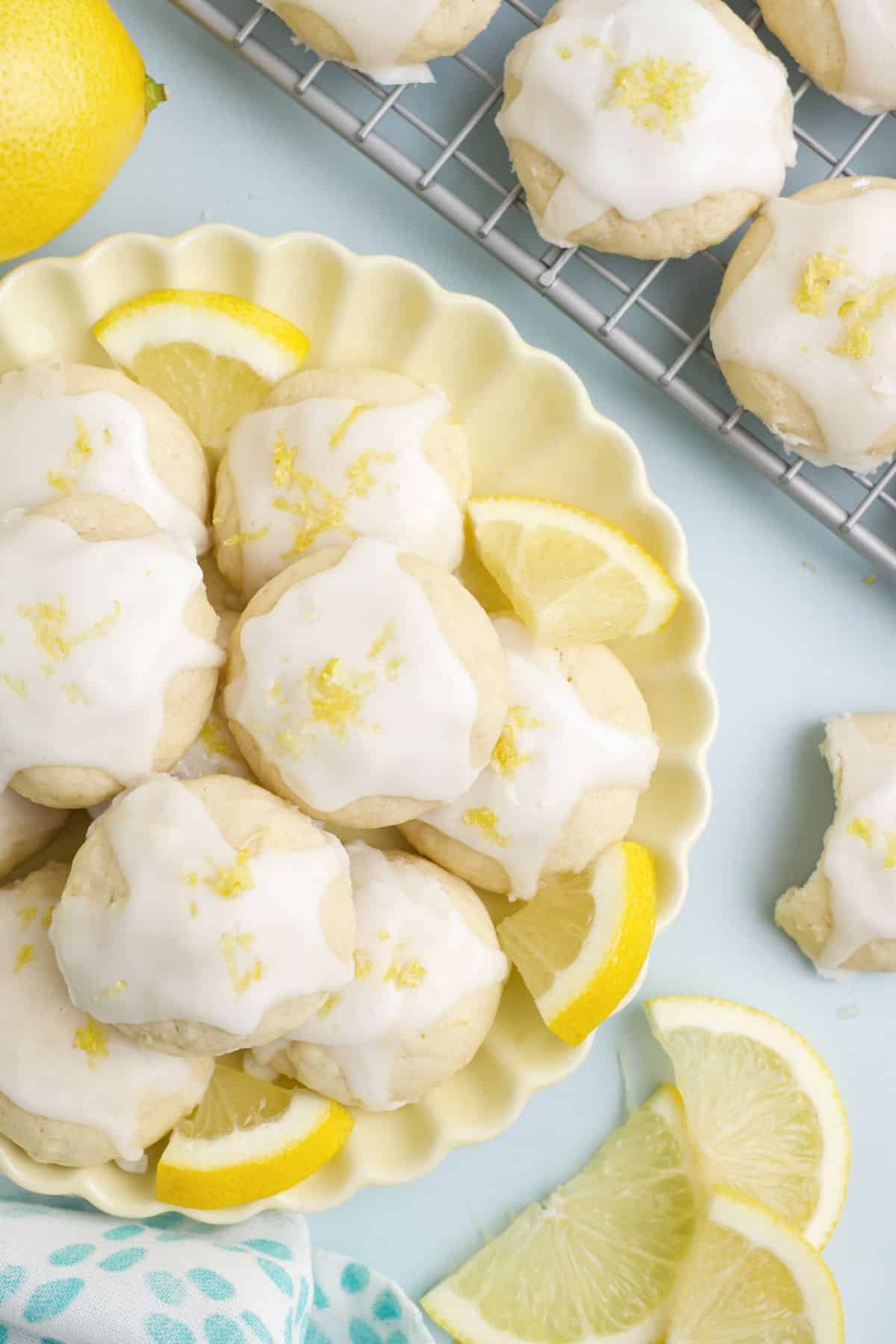 A yellow plate with lemon cookies on it and a few cookies on the table surface around it.