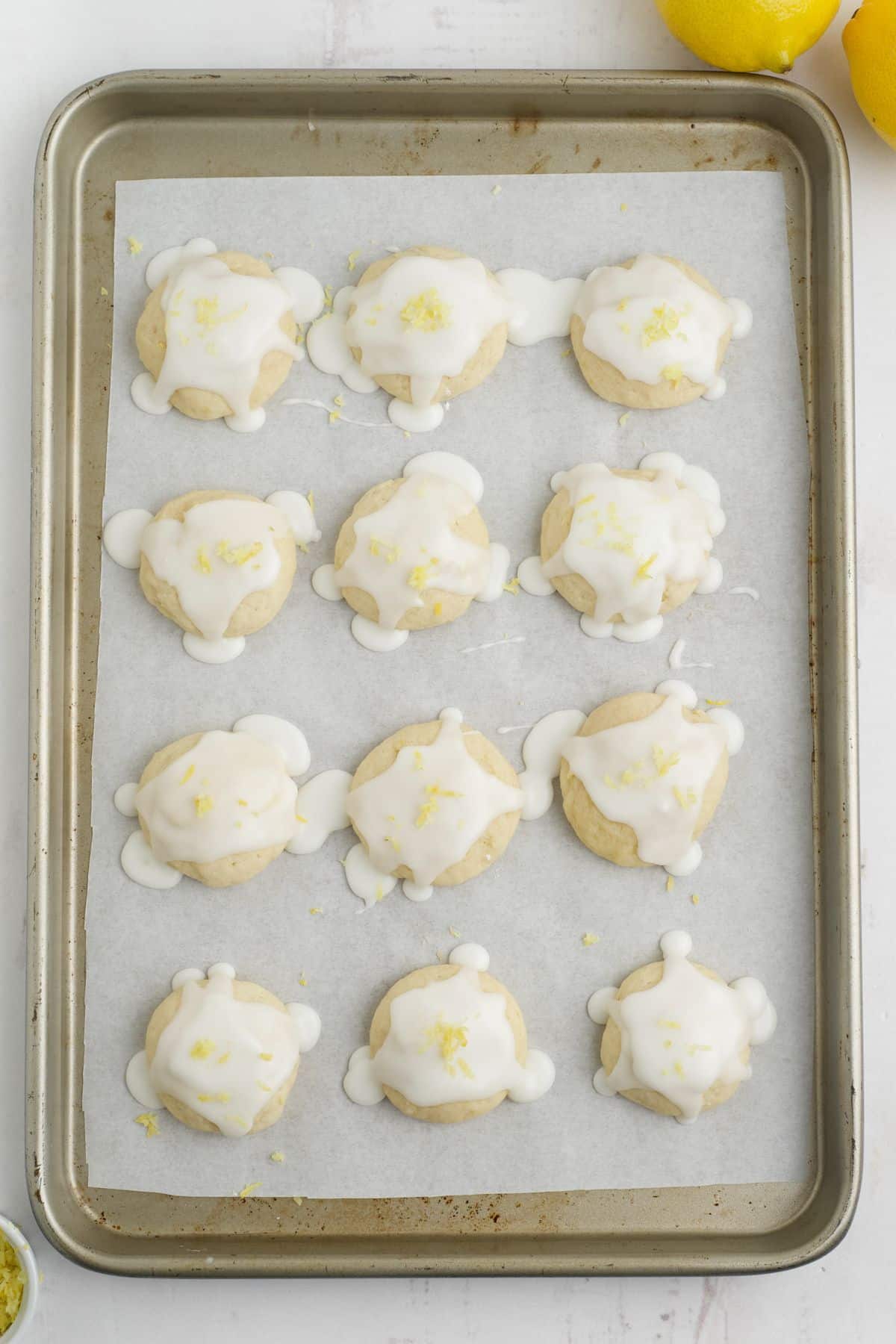 Lemon cookies on a baking tray with glaze added and lemon zest sprinkled on top.