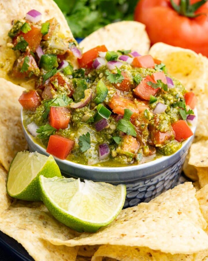 A chip dipping into a bowl of salsa pesto surrounded by tortilla chips.