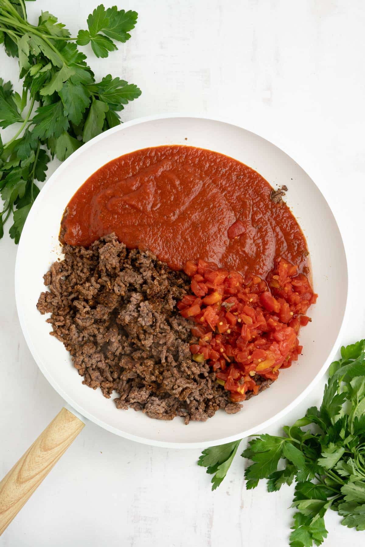 Beef in a skillet with tomato sauce and tomatoes added.