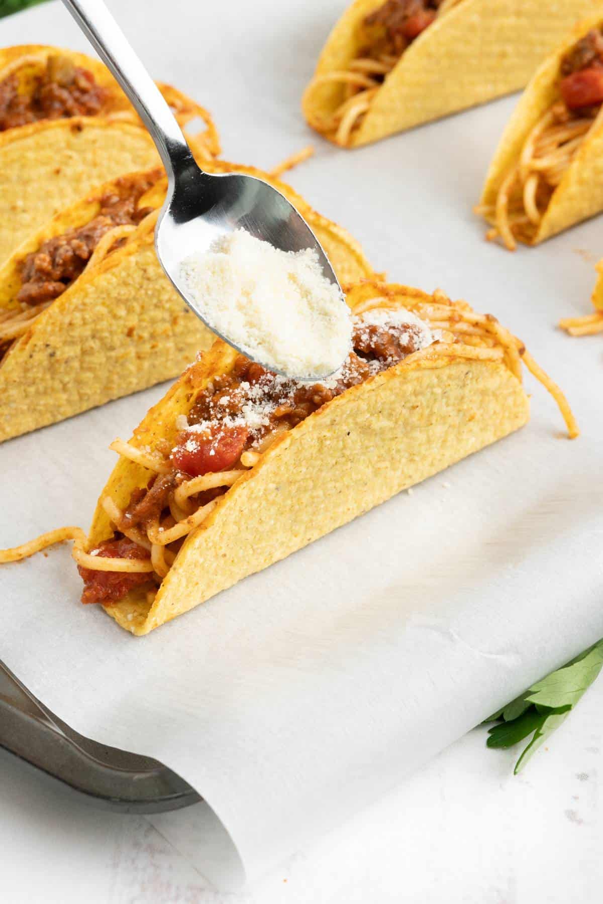 A spoon adding parmesan to the top of a taco with spaghetti.
