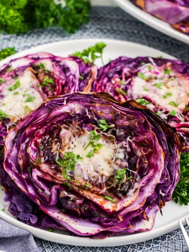 Roasted red cabbage steaks on a plate on the table with a platter in the background.