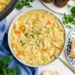 A bowl of crockpot creamy chicken noodle soup on a table surrounded by sprigs of parsley.