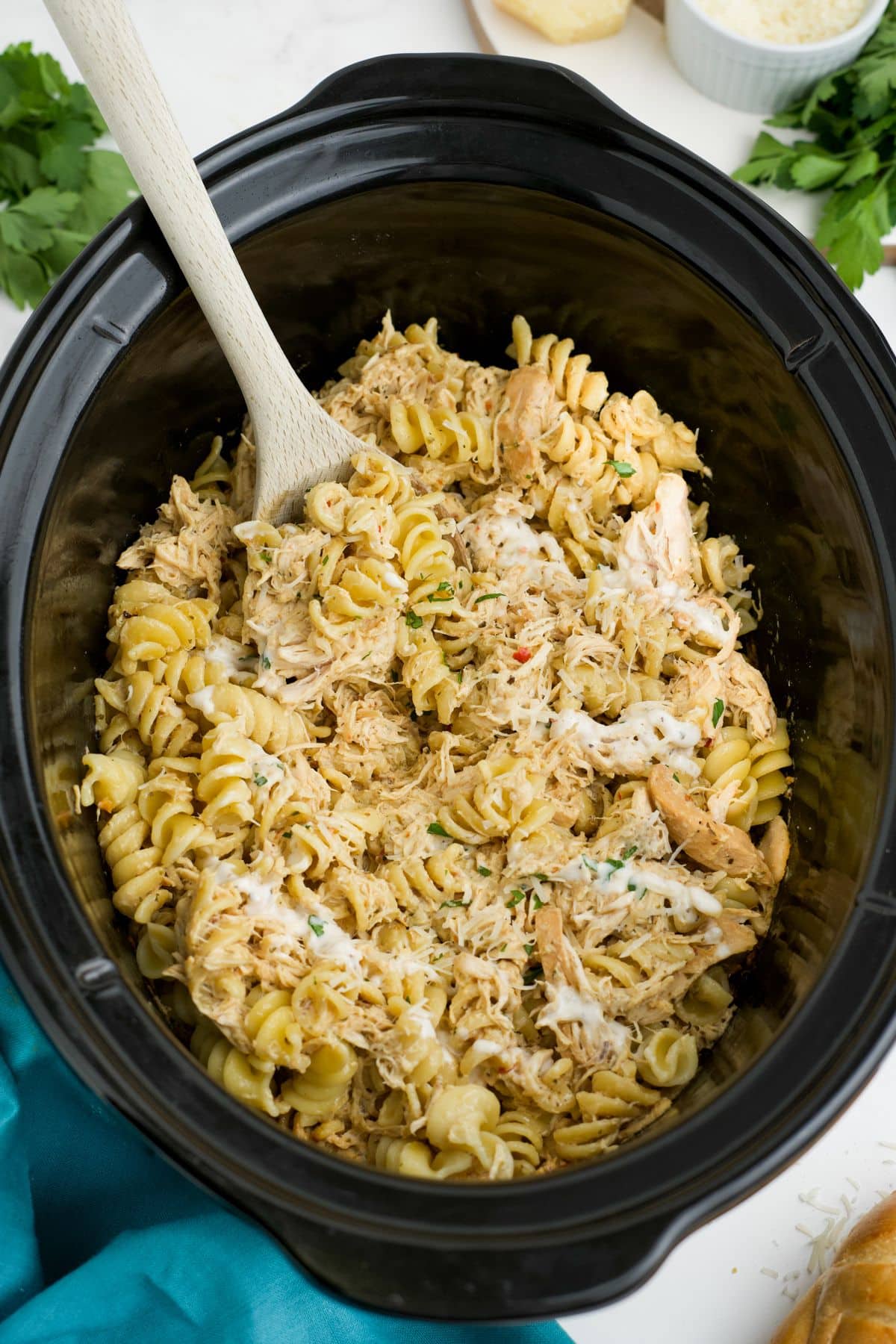Garlic parmesan chicken and pasta in a slow cooker with a wooden spoon resting on the side.