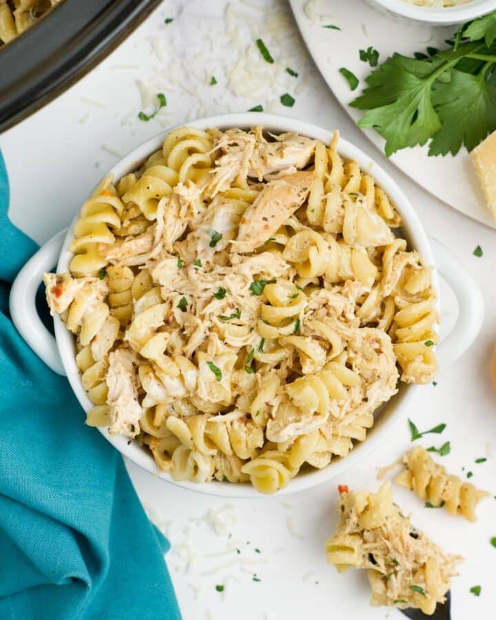 Crockpot garlic parmesan chicken pasta in a bowl on the table with more in the slow cooker.