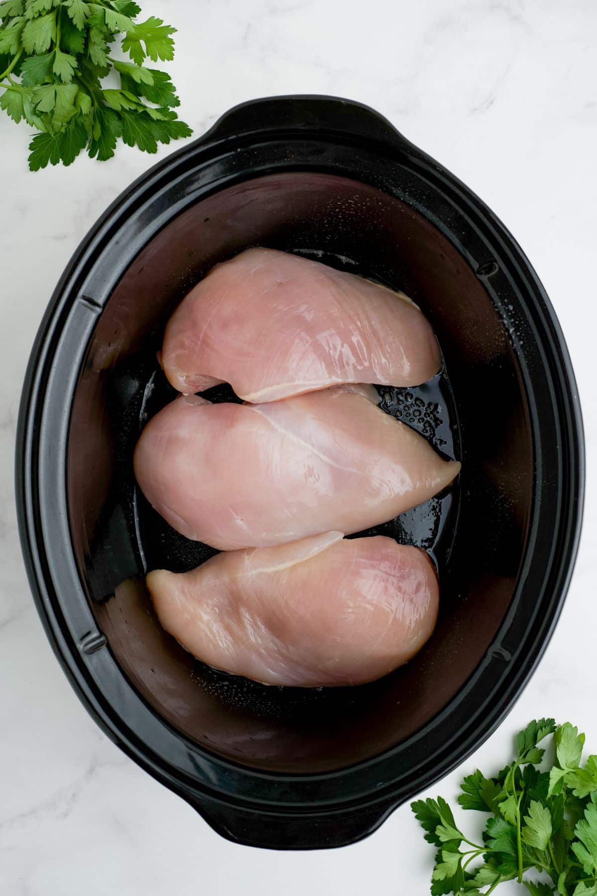 Raw chicken in the bottom of a slow cooker.