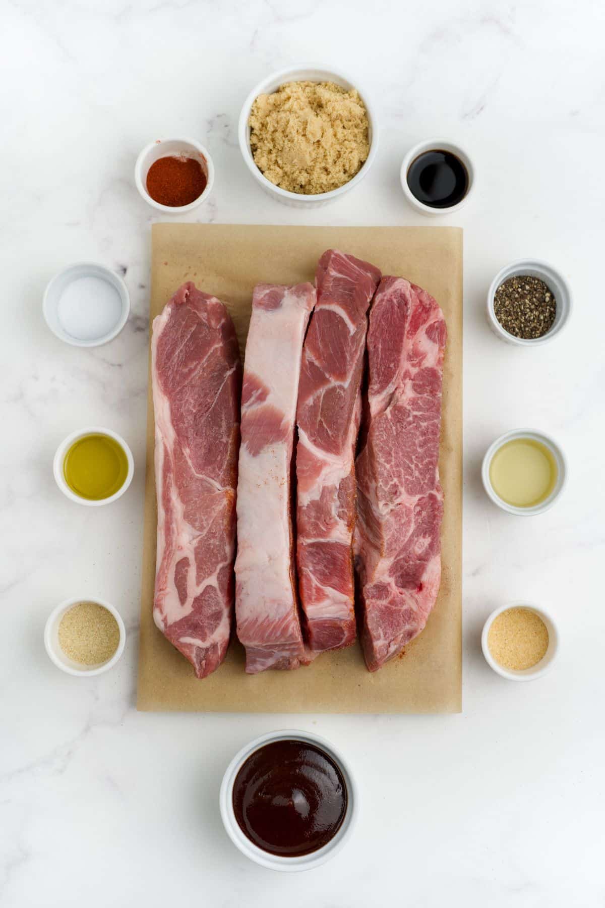 Pork ribs on a cutting board surrounded by small bowls of the seasonings and ingredients used to flavor them.