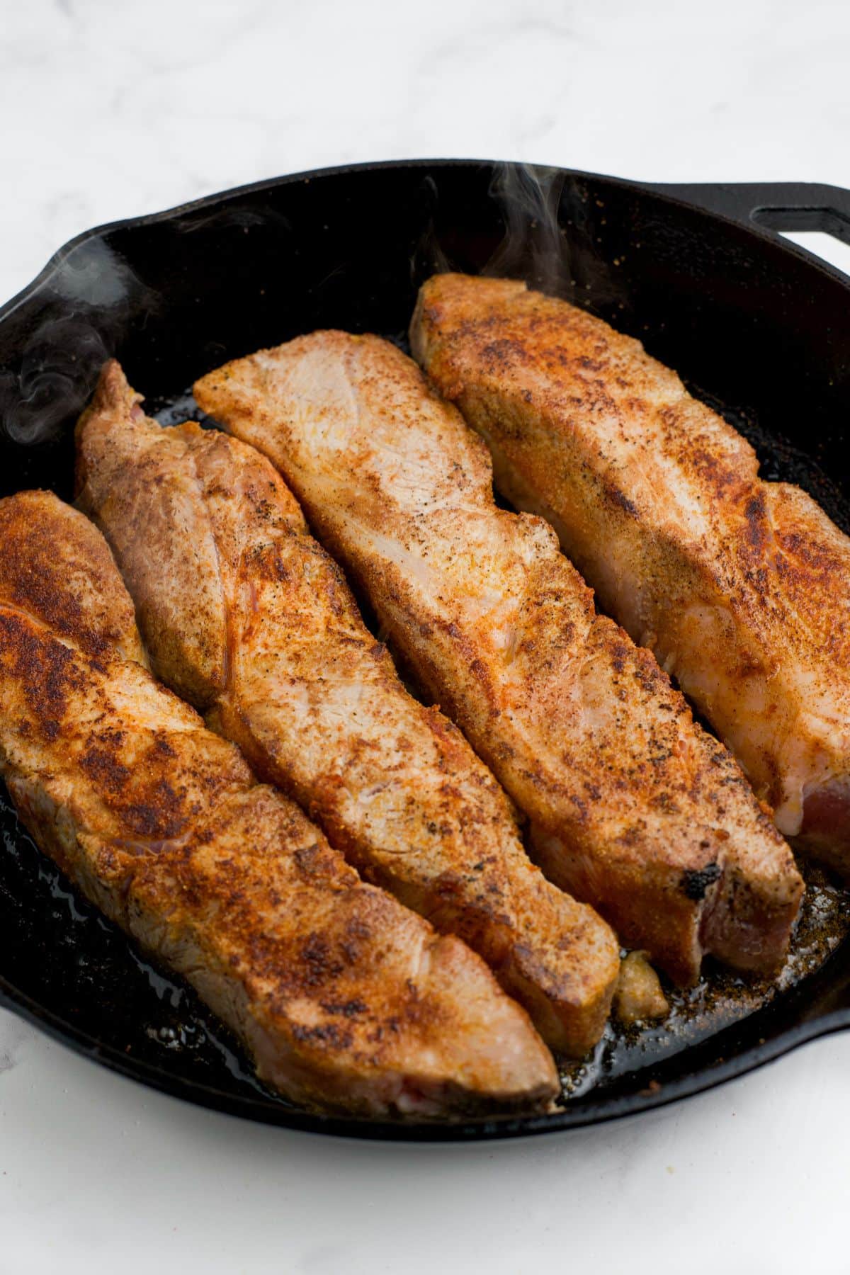 Seasoned pork ribs in a skillet to sear.