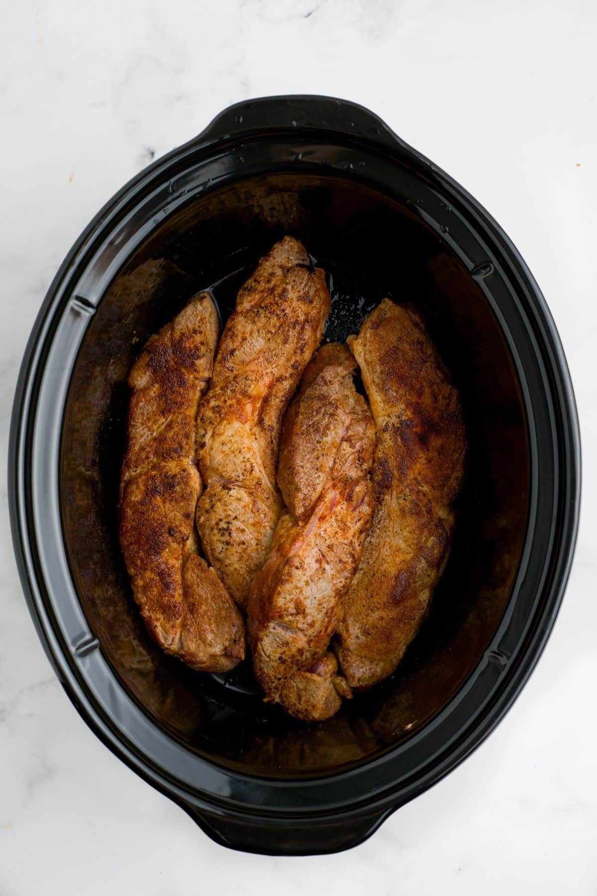 Seared pork ribs added to a slow cooker.