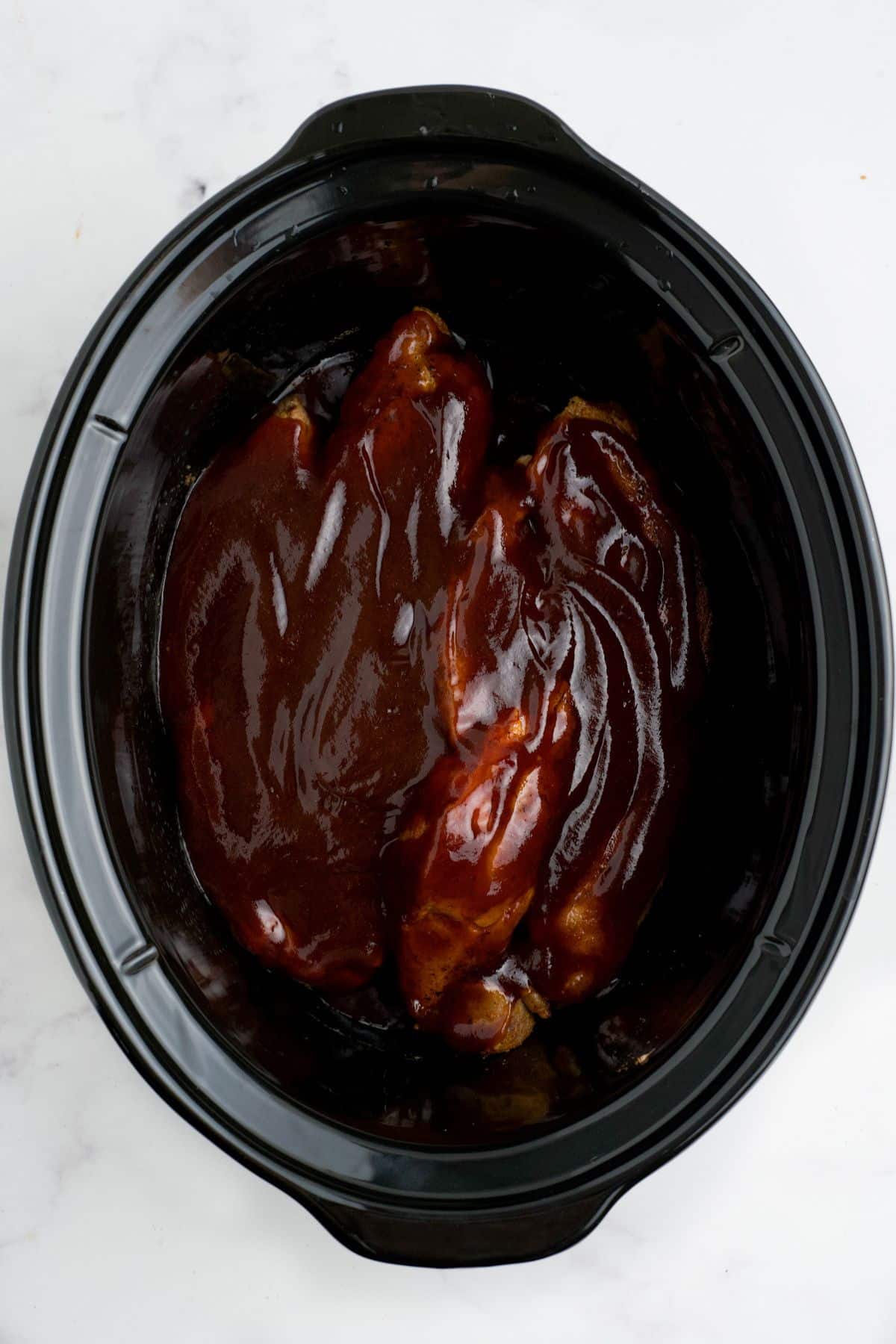 BBQ sauce poured over the top of the boneless pork ribs in a slow cooker.