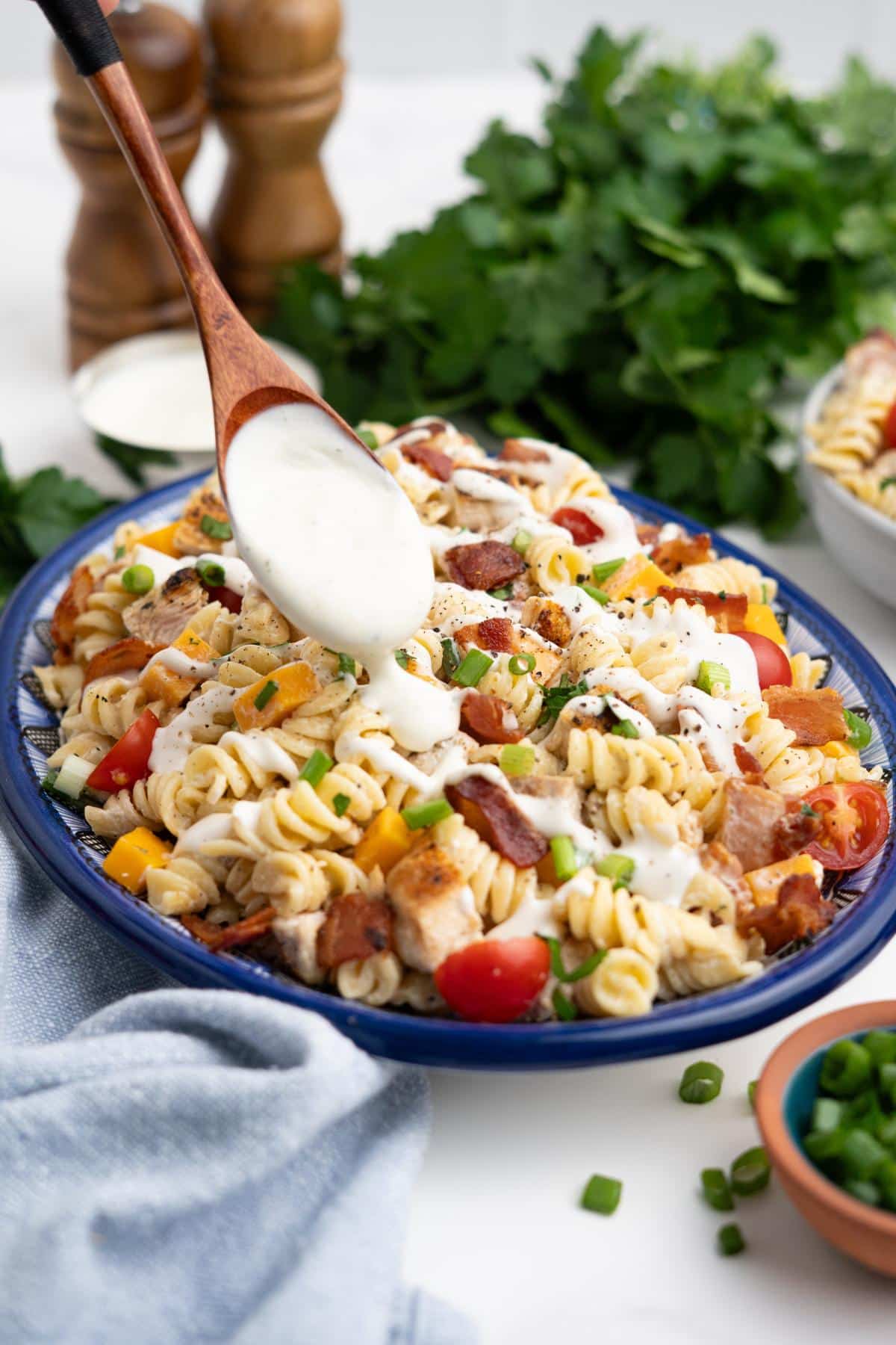 A wooden spoon drizzling more dressing on a ranch pasta salad.