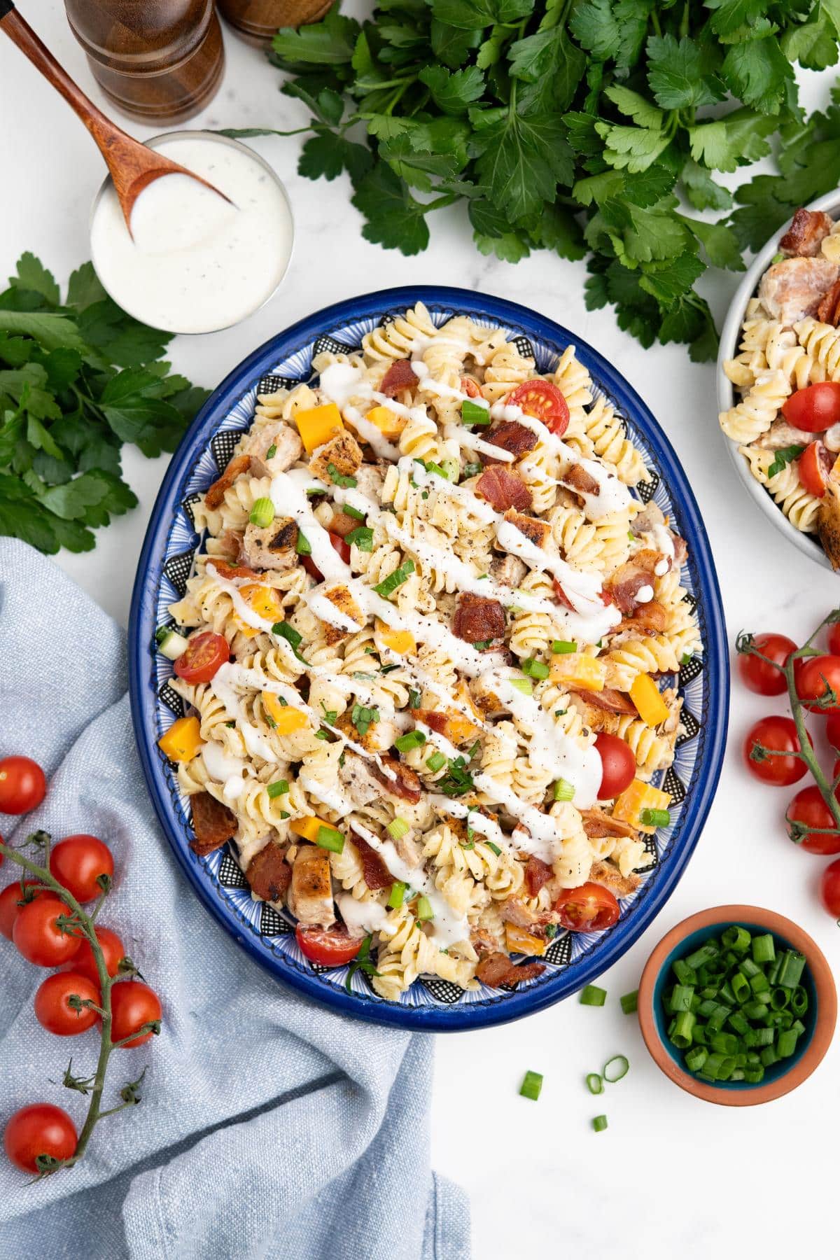 A platter of chicken bacon ranch pasta salad on a table with fresh vegetables scattered around.