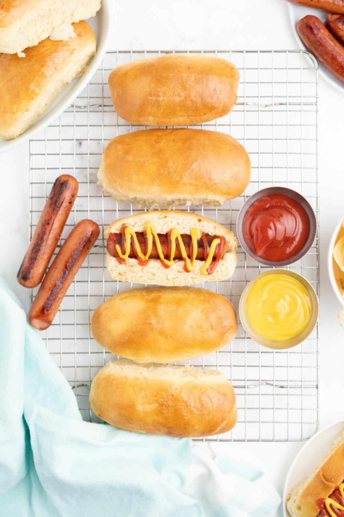 Homemade hot dog buns on a wire rack with a hot dog in a bun in the middle.