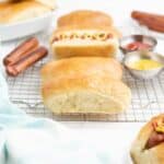Homemade hot dog buns on a table with condiments and grilled hot dogs.