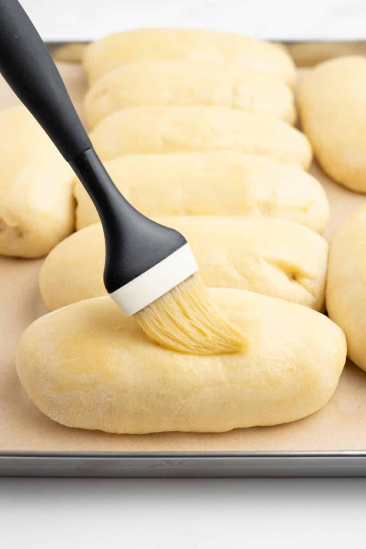 Brushing the hot dog bun dough with a pastry brush and egg wash.