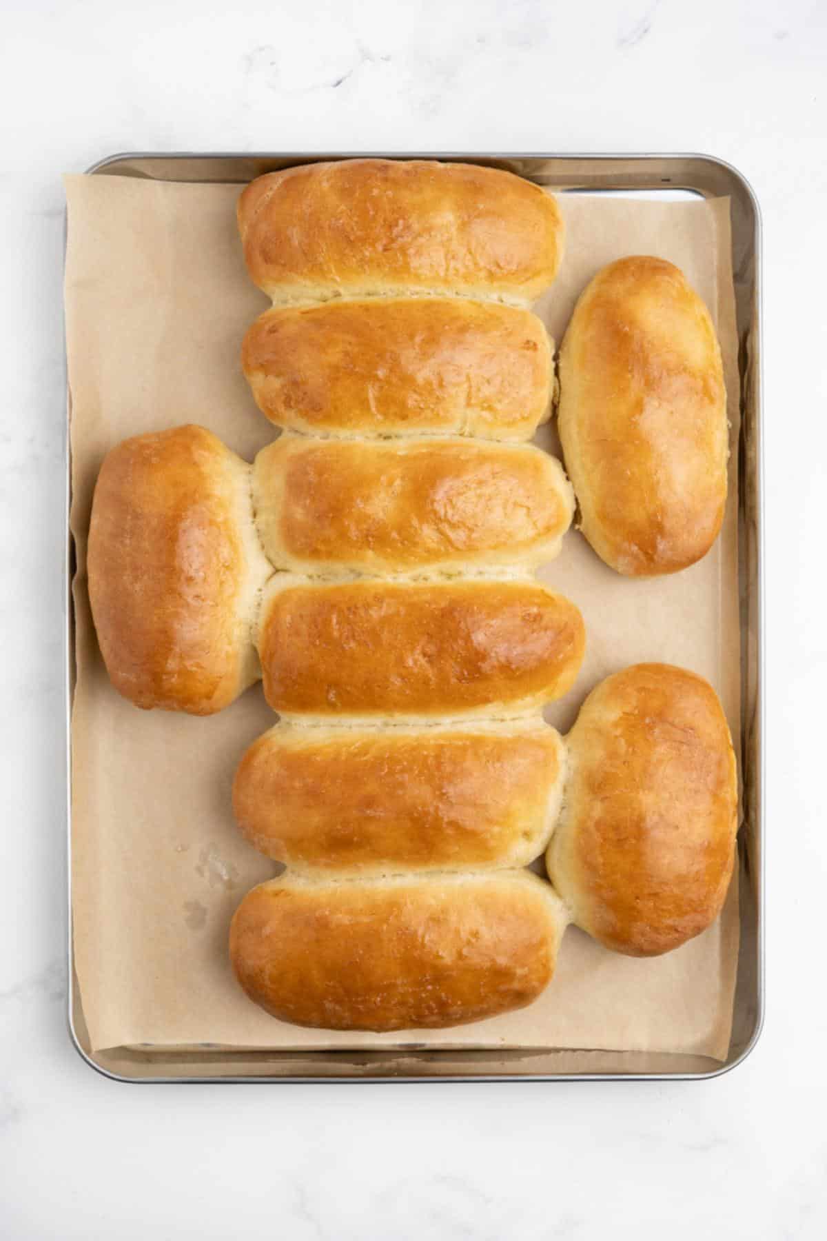 Baked hot dog buns on a baking tray with golden brown tops.