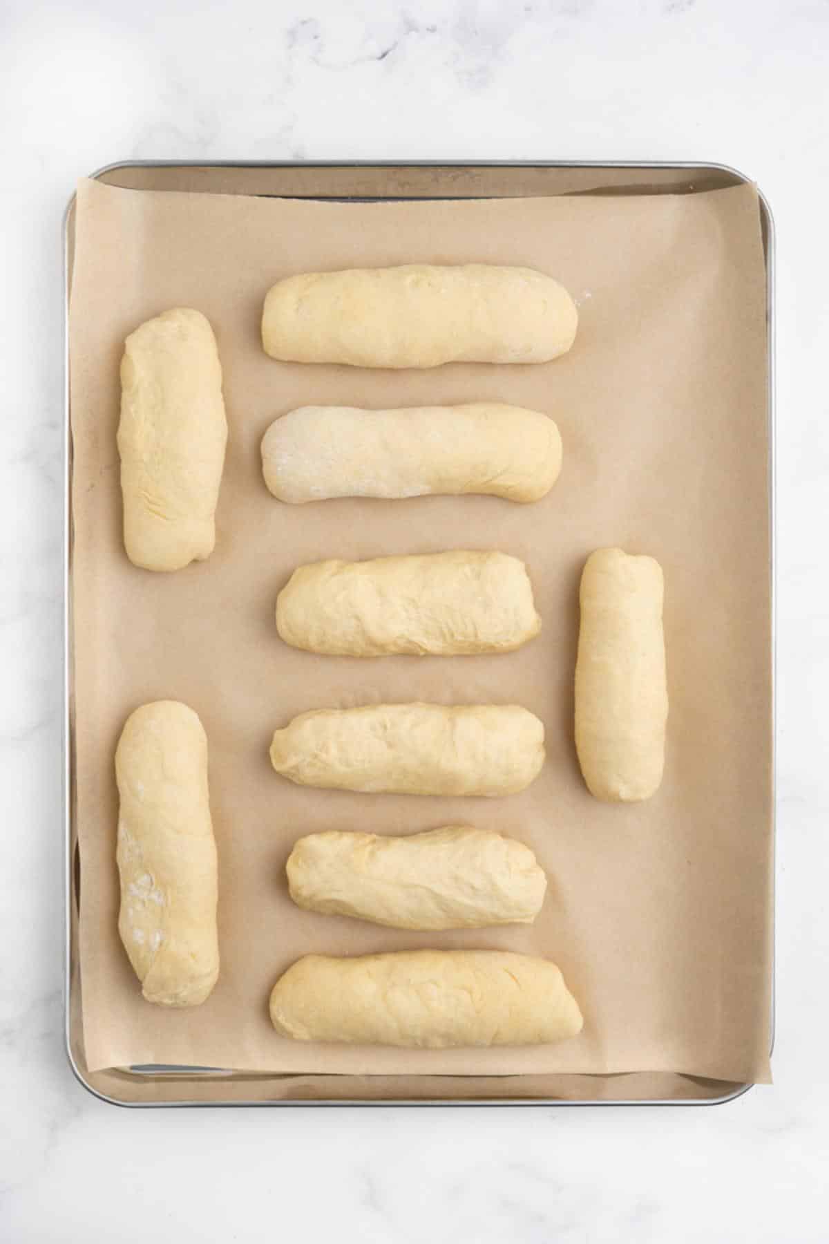 Raw dough shaped into hot dog buns on a baking tray to proof again.