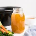 A jar of slow cooker rotisserie chicken broth in front of a slow cooker.