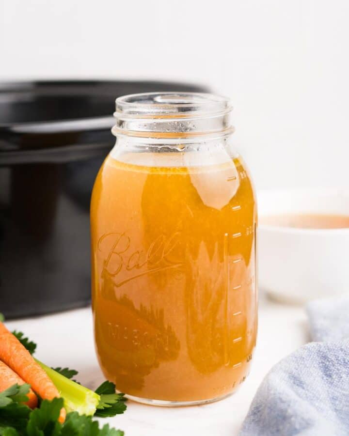A jar of slow cooker rotisserie chicken broth in front of a slow cooker.