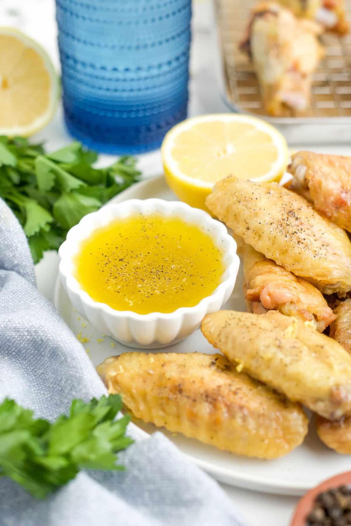 A small bowl of lemon pepper sauce next to a chicken wings on a plate.