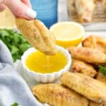 A hand dipping a chicken wing into lemon pepper sauce.