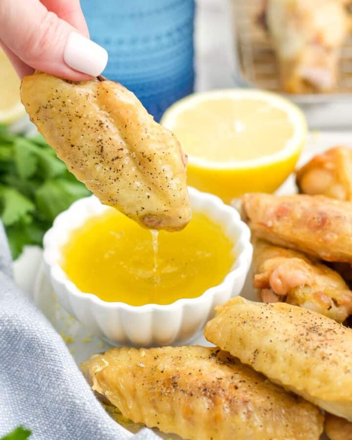 A hand dipping a chicken wing into lemon pepper sauce.