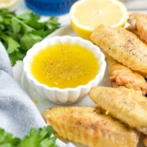 A bowl of lemon pepper sauce next to some chicken wings on a plate.