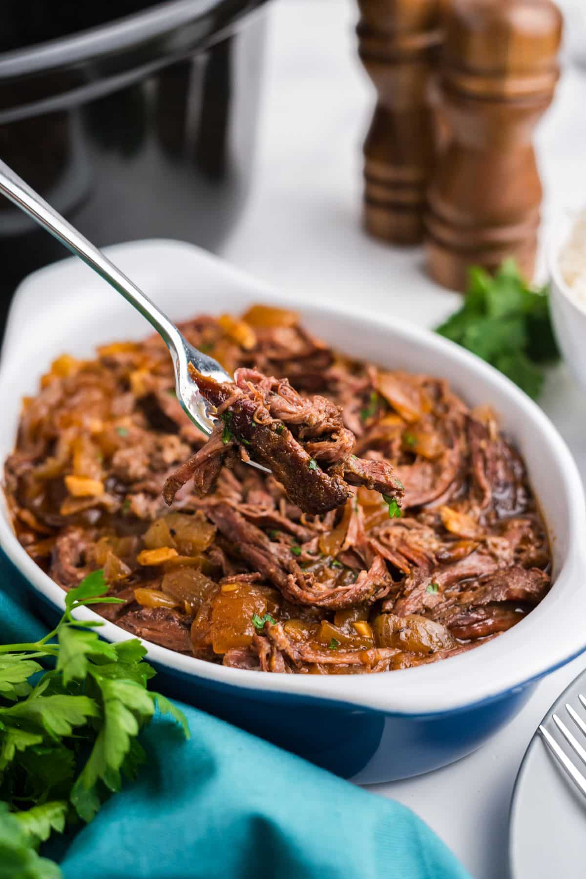 Shredded slow cooker skirt steak in a dish with a fork holding up a bite.