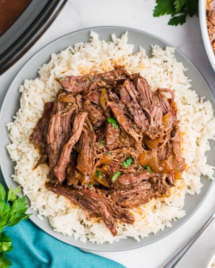 Crockpot skirt steak shredded and served over a plate of rice.