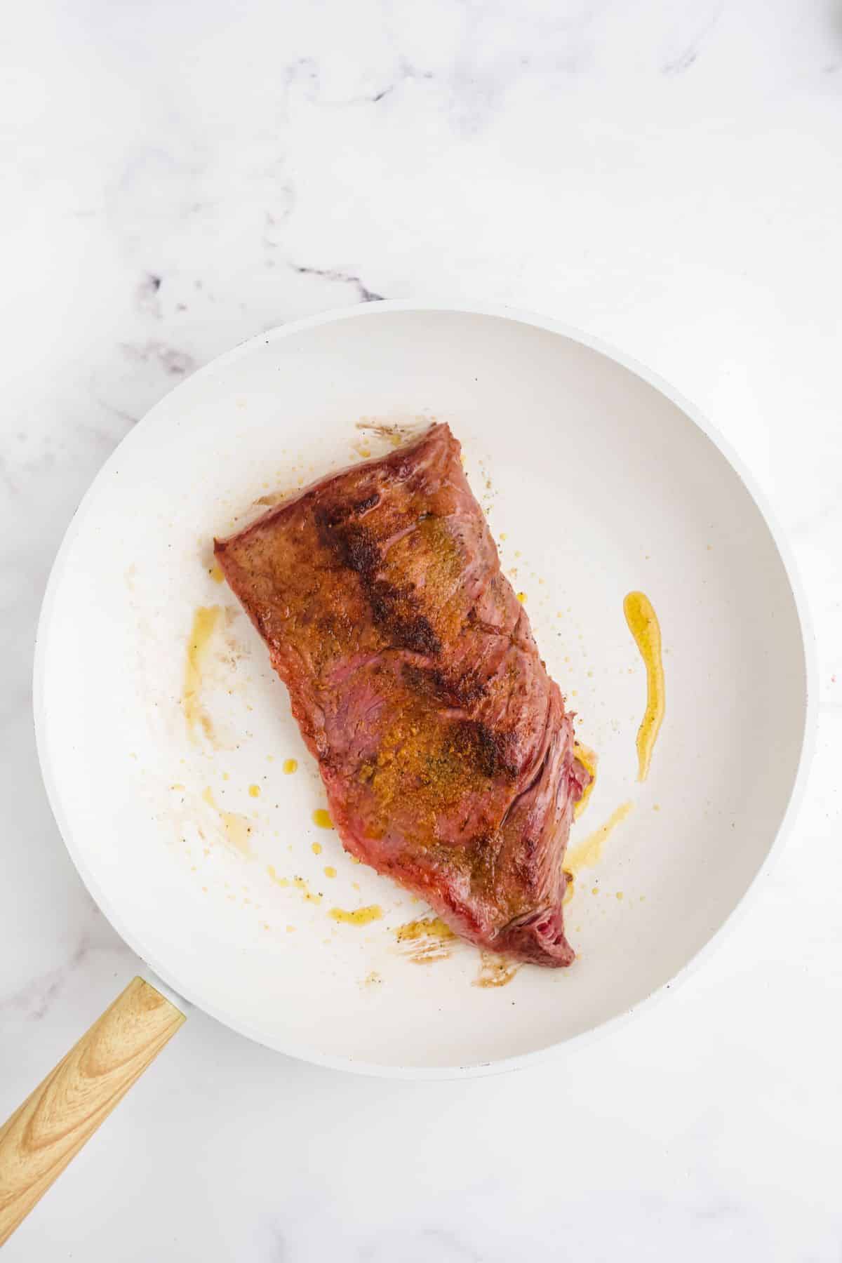 Seared skirt steak in a white skillet.