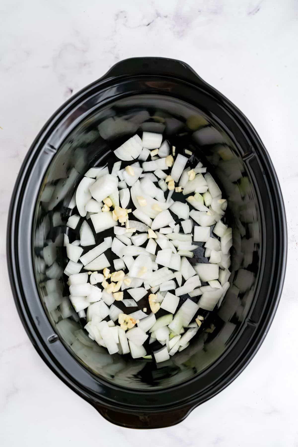 Onions in the bottom of a slow cooker.