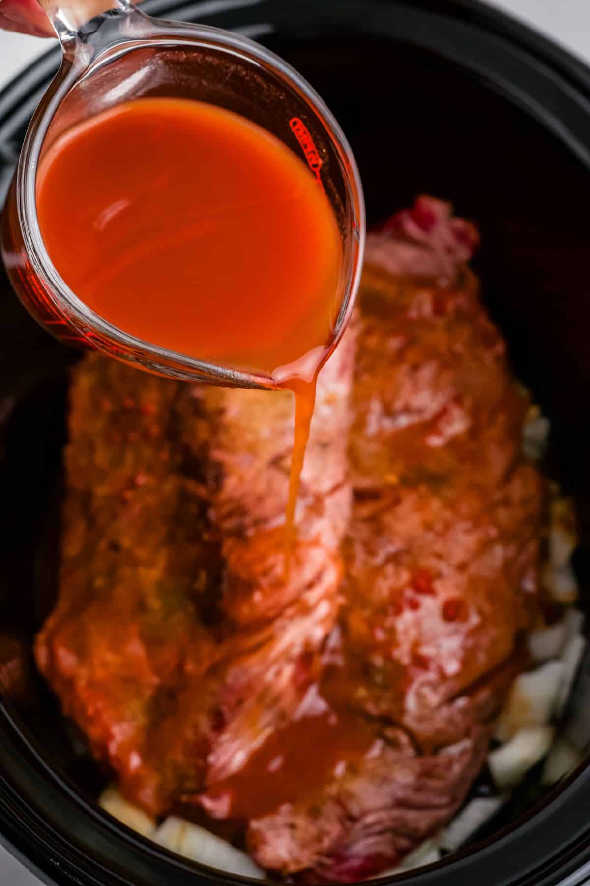 Adding the sauce over the steak and onions in the crockpot.