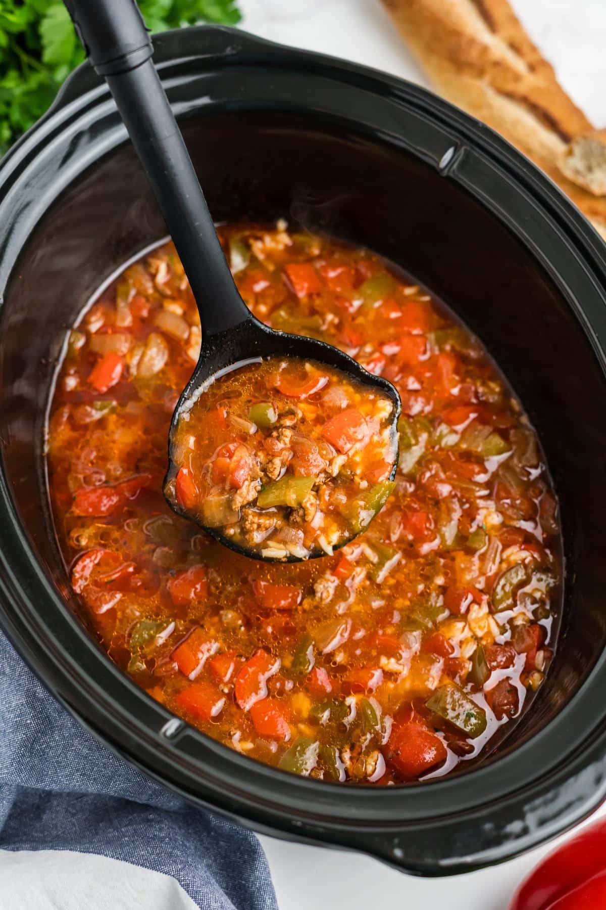 A ladle lifting a serving stuffed bell pepper soup from a slow cooker.