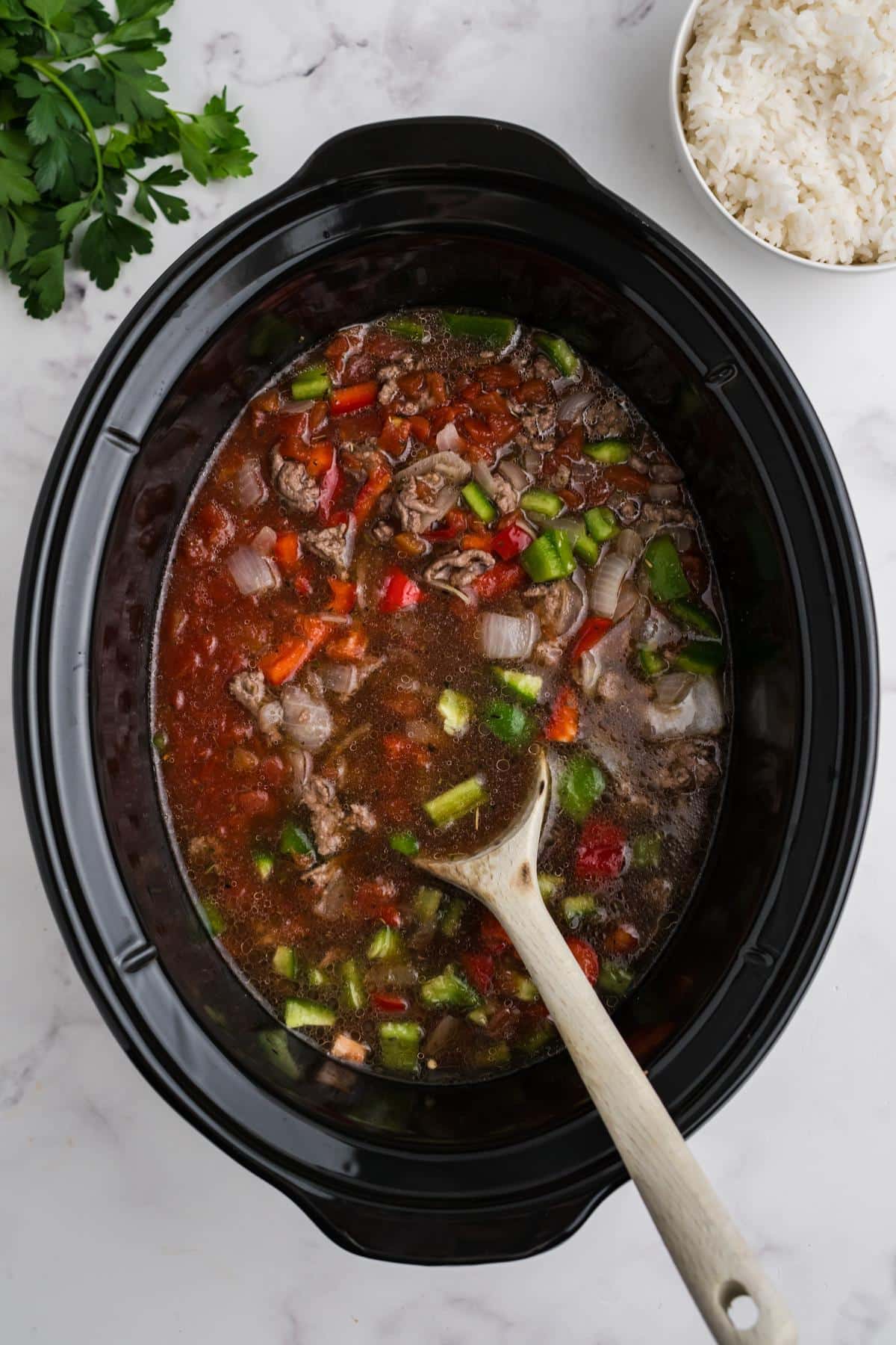 Stuffed pepper soup in a slow cooker with a wooden spoon.