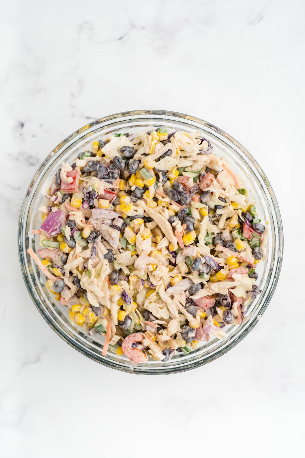 An image of southwest coleslaw after being tossed in dressing. Image is overhead in a clear bowl.
