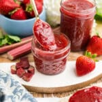 An image of strawberry and rhubarb preserves in a small jar with a spoon.