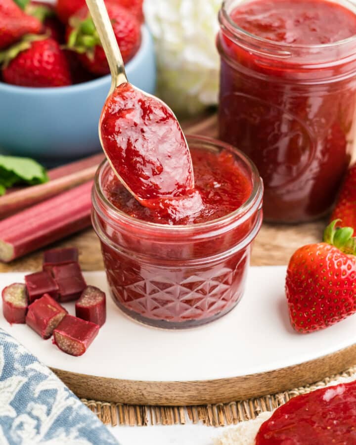 An image of strawberry and rhubarb preserves in a small jar with a spoon.