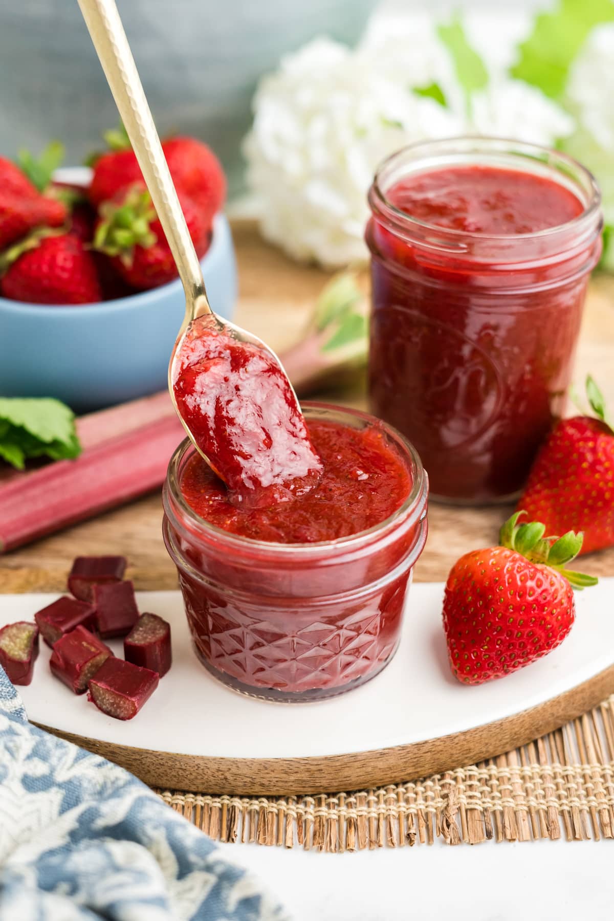 An image of strawberry rhubarb preserves in a small jar with a spoon scooping up the strawberry rhubarb jam