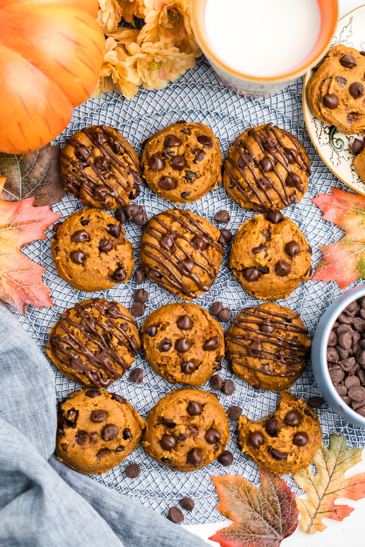 An overhead image of a batch of pumpkin chocolate chip cookies. Some with chocolate chips and others with chocolate drizzle.