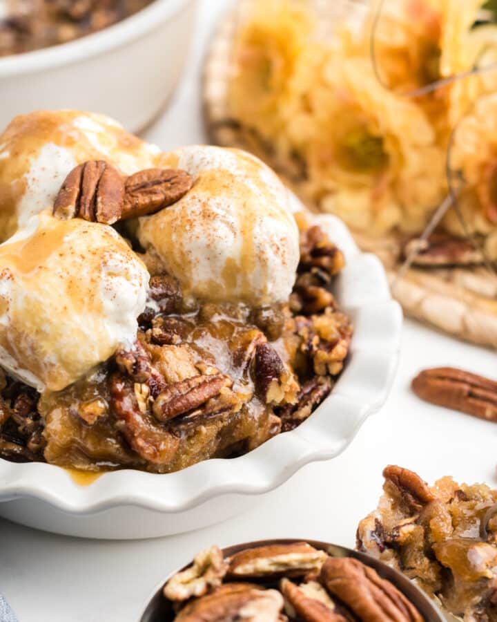 An image of hote pecan pie cobbler in a small white dish with 3 scoops of vanilla extract.