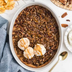 Overhead image of pecan pie cobbler in an oval casserole dish with 3 scoops of ice cream.