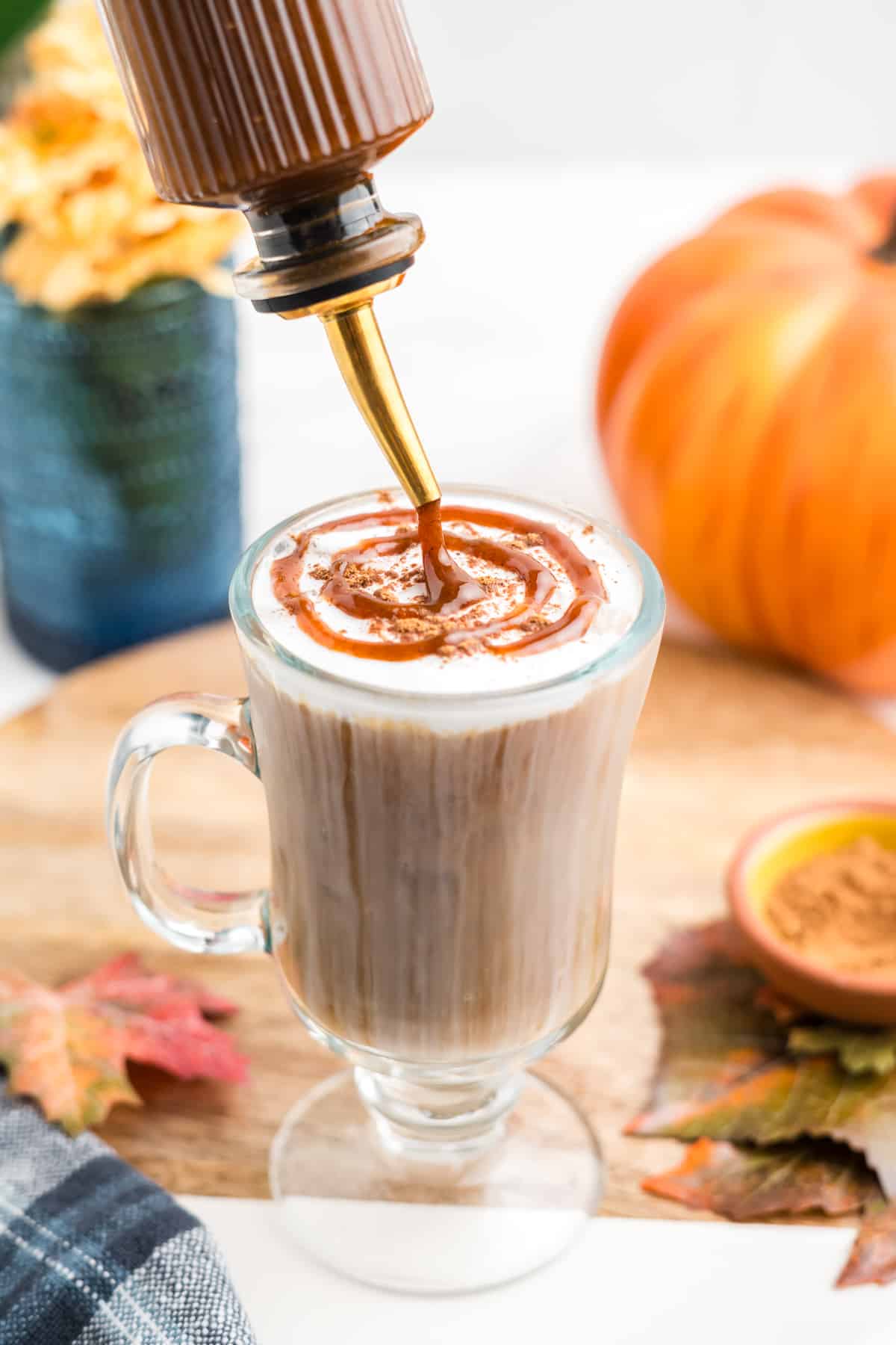 An image of fresh pumpkin spice syrup being poured over ice coffee with a sweet cream foam topping. 