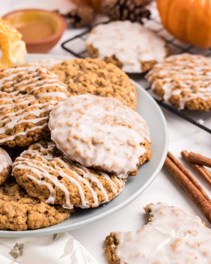 A plate full of glazed pumpkin oatmeal cookies on a plate with fall decor around.
