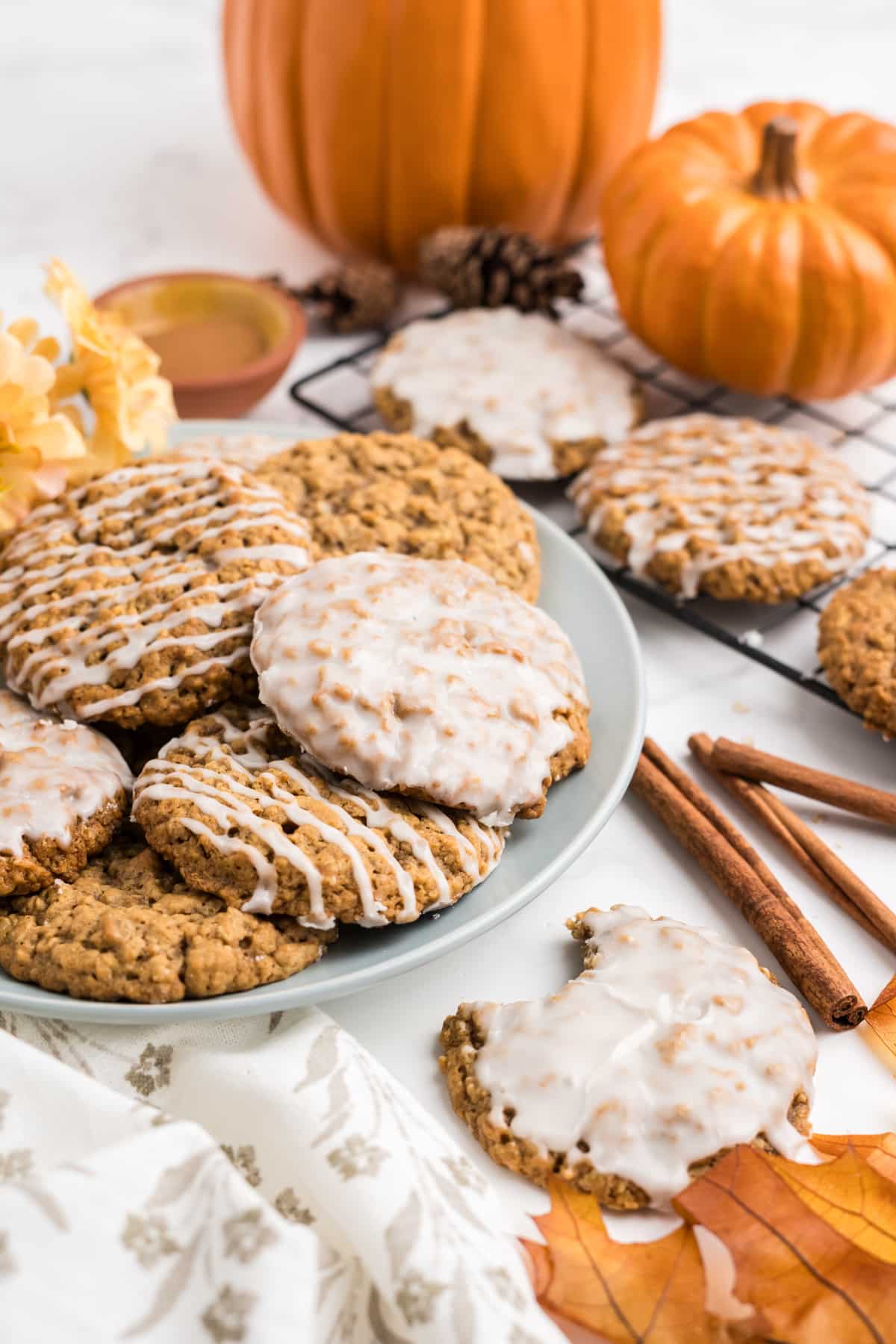 Glazed Pumpkin Oatmeal cookies stacked on a plate with fall decor surrounding them. 