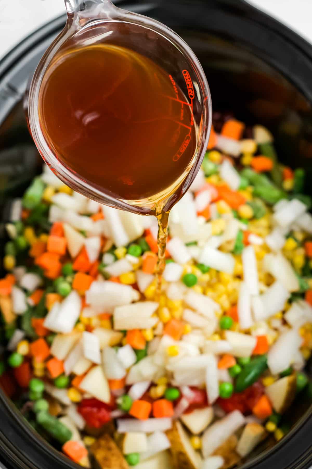 Broth being poured on top of the other ingredients in the slow cooker.