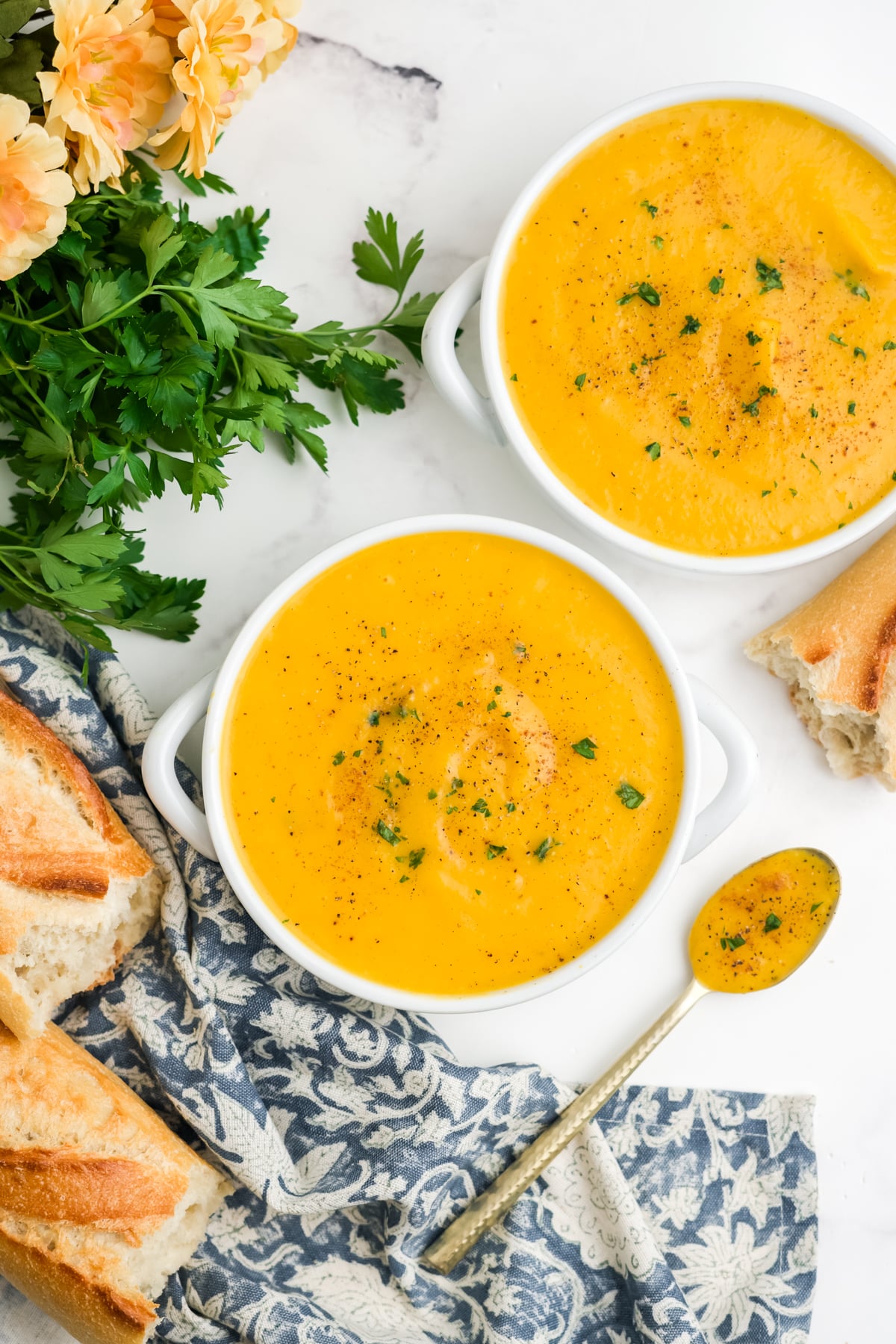 Two bowls of roasted butternut squash soup with a spoonful resting on the side. 