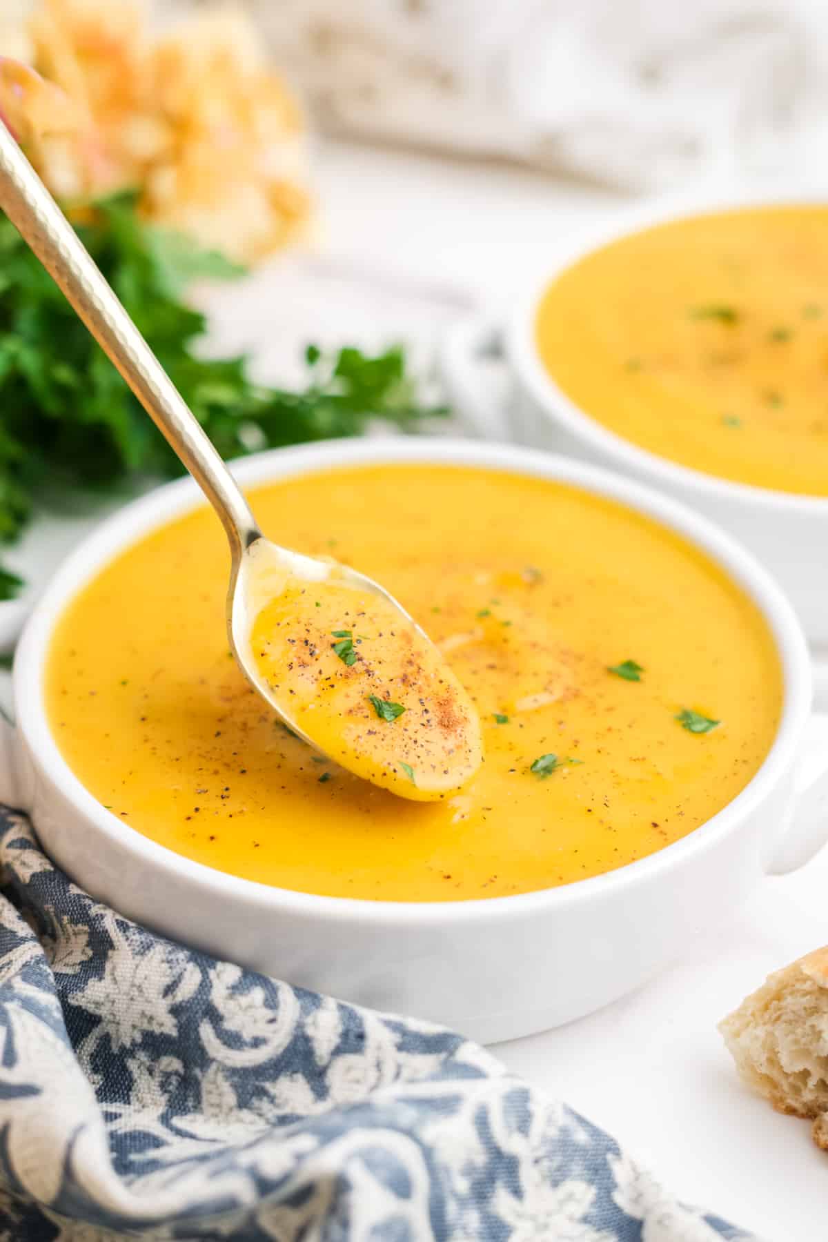 Butternut squash soup in a bowl with a spoonful held up over the bowl. 