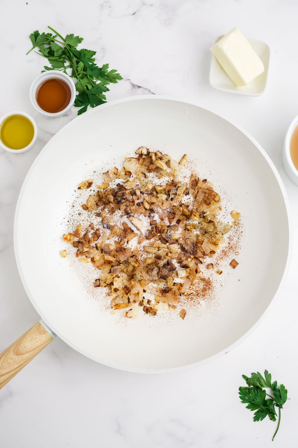Onions and garlic cooking in a white skillet.