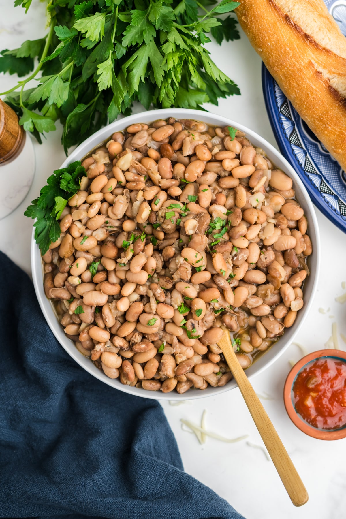 A bowl of crockpot pinto beans on a table with a wooden spoon resting in the bowl.
